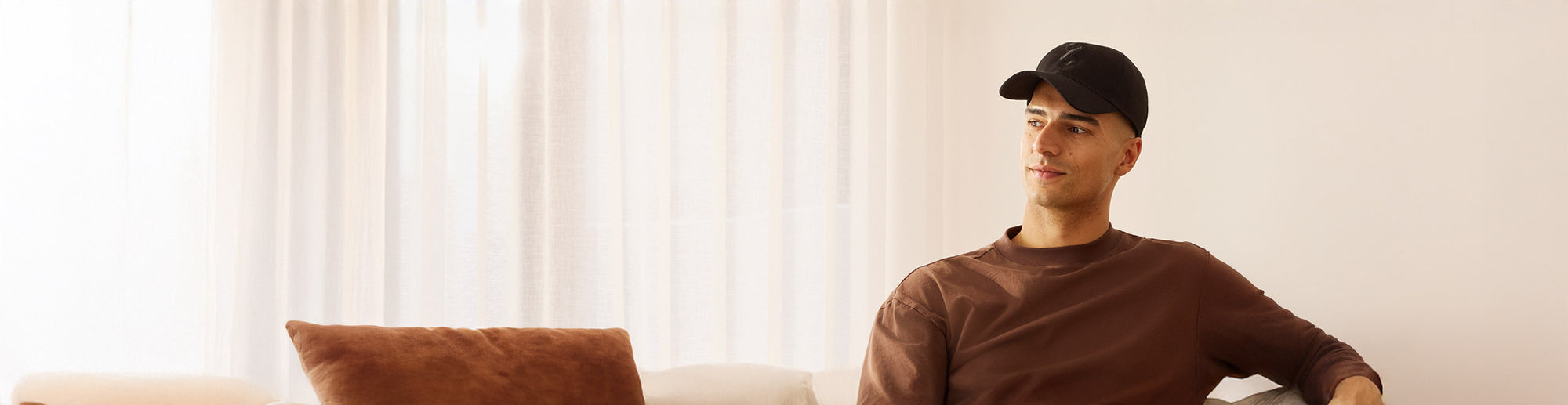 Man wearing red light cap and brown sweater sitting on a couch with a neutral background